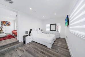 A modern bedroom with a white bed, a red chair, a TV, and a painting on the wall. - Tropical 3BR Miami Getaway – Pool & Prime Location (Miami)
