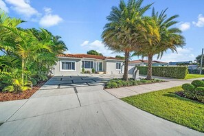 A residential house with a paved driveway, palm trees, and a well-maintained lawn. - Tropical 3BR Miami Getaway – Pool & Prime Location (Miami)