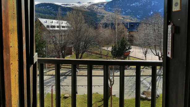 Vista desde una ventana con barandilla de metal, una montaña nevada y edificios al fondo.