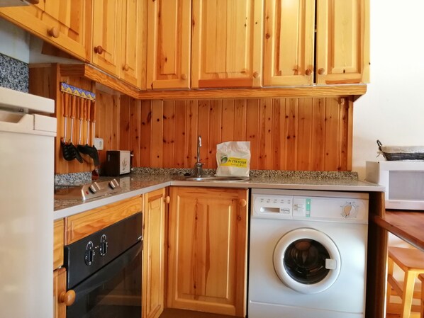 A kitchen with wooden cabinets, a dishwasher, a washing machine, and a microwave. - South facing and sunny apartment - Falcó 17 (Pla de l'Ermita)