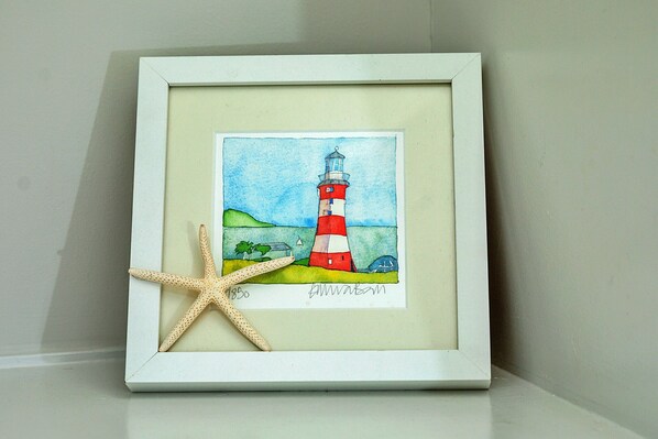 A framed artwork of a lighthouse with a starfish, signed by the artist.