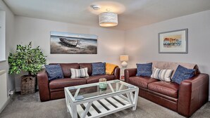 A living room with two brown leather sofas, a glass coffee table, a potted plant, and two wall-mounted paintings. - Old Salt Loft (Whitby)