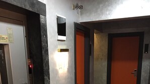 A hallway with a textured carpet, a door with a red handle, and a wall-mounted light fixture. - Acar Suite Hotel (Istanbul)