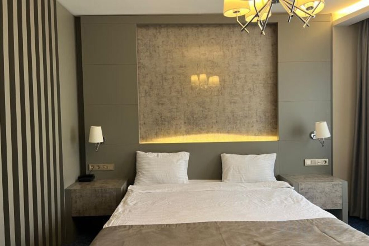 Habitación de hotel con una cama grande, dos mesitas de noche, un cabecero moderno y lámparas de pared.