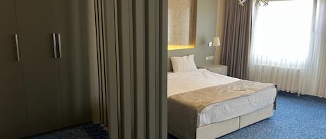 Een hotelkamer met een groot bed, een kledingkast, een nachtkastje, een lamp en een raam met gordijnen.