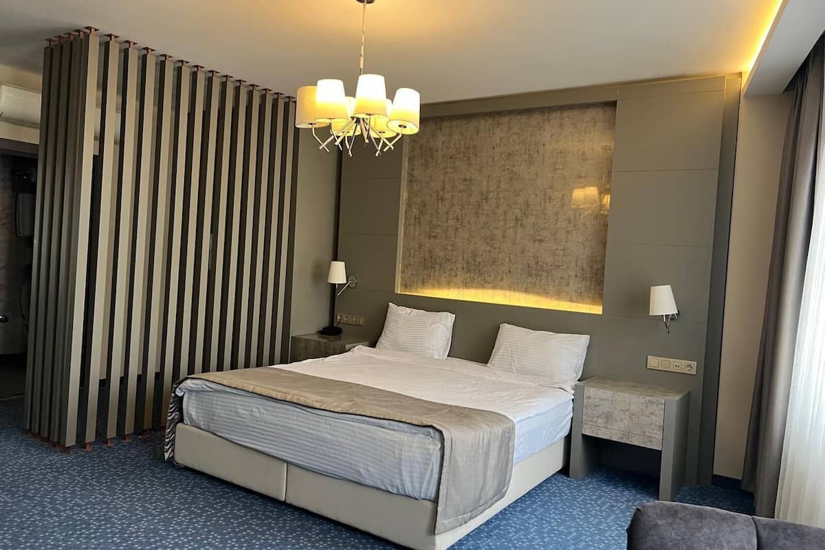 Quarto de hotel moderno com uma cama grande, um candelabro, parede texturizada e carpete estampado.