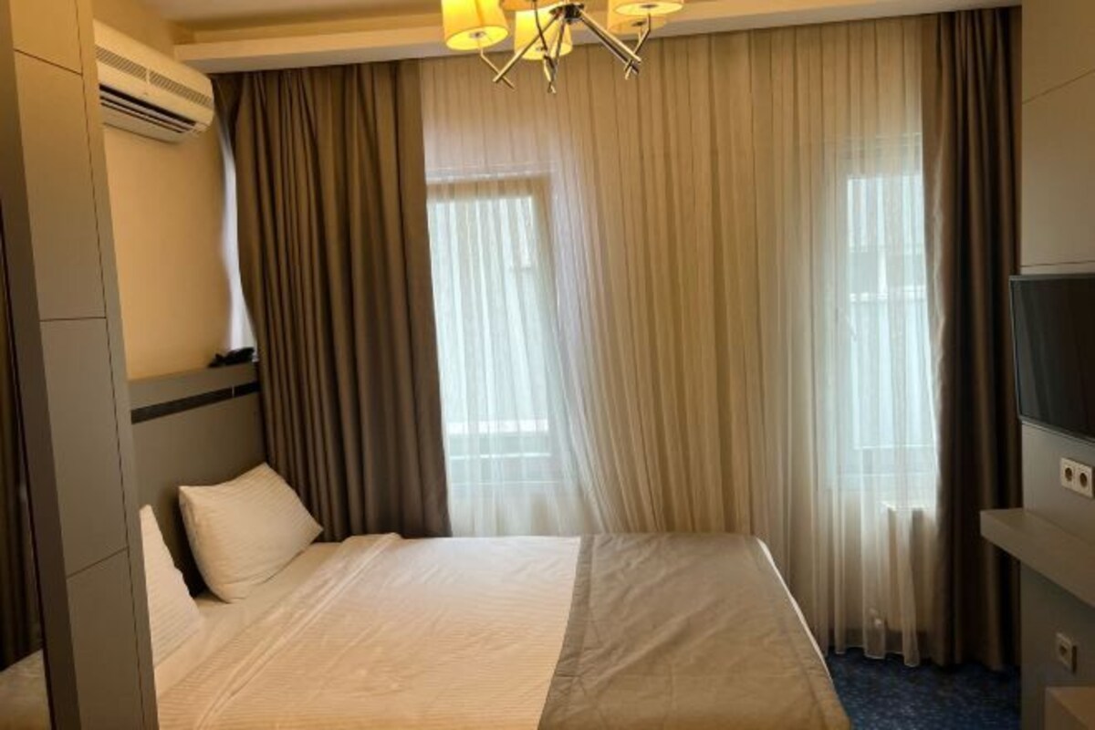 Una habitación de hotel con una cama, cortinas, un televisor y un equipo de aire acondicionado.