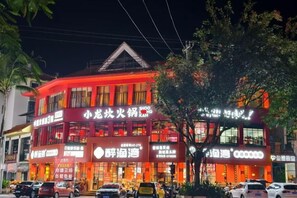A multi-story building with illuminated signage, a red facade, and a visible entrance. - Mancheng Boutique Hotel (Mengla)