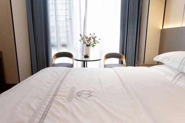 A hotel room with a large bed, two chairs, a small table with a vase of flowers, and a window with curtains.