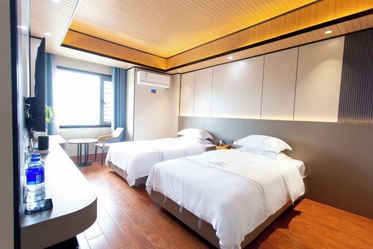 A hotel room with two beds, a desk, a chair, and a TV.