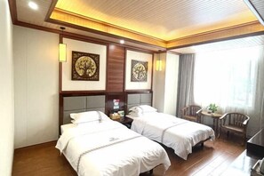 A hotel room with two beds, wooden headboards, a small table with chairs, and artwork on the walls. - Mancheng Boutique Hotel (Mengla)