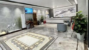 A modern lobby with a reception desk, a large TV screen, decorative wall art, and a patterned carpet. - Mancheng Boutique Hotel (Mengla)