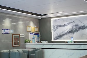 A reception area with a marble counter, framed certificates, and a large wall mural. - Mancheng Boutique Hotel (Mengla)