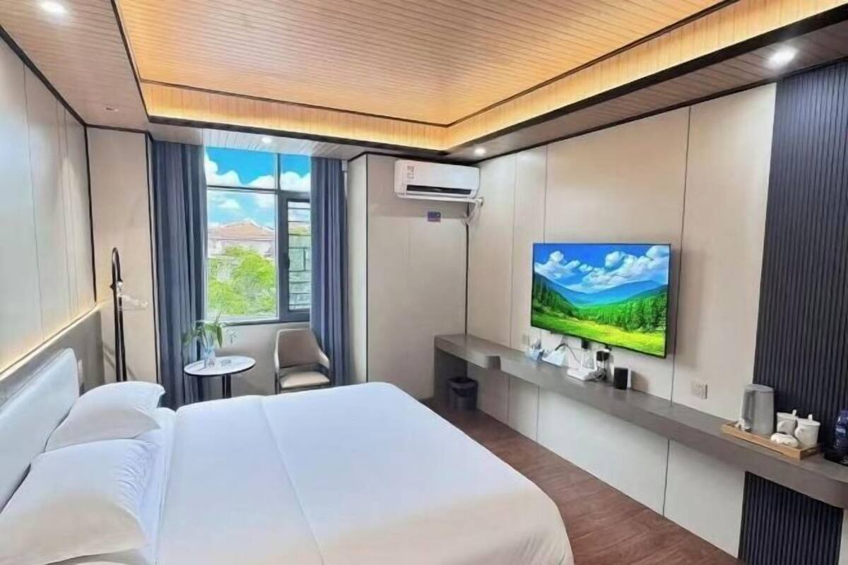 A hotel room with a bed, a TV, a small table, and a window with curtains.