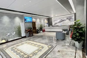 A hotel lobby with a reception desk, a flat-screen TV, a large painting, and a patterned carpet. - Mancheng Boutique Hotel (Mengla)