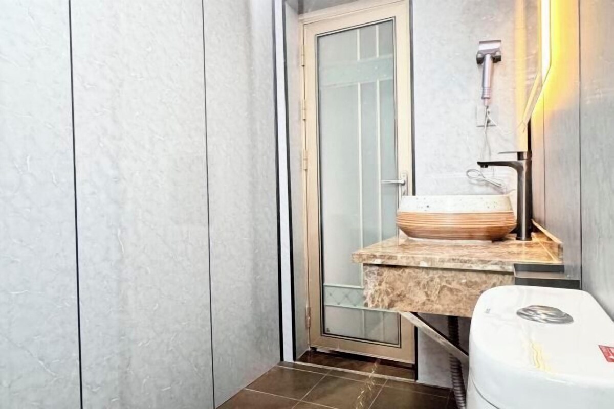 A bathroom with a glass door, a sink with a marble countertop, and a white toilet.
