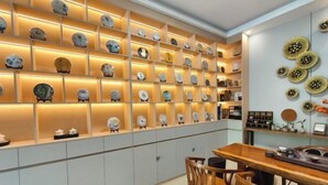 A dining area with a wooden table and chairs, a wall with shelves displaying clocks, and decorative wall art. - Mancheng Boutique Hotel (Mengla)