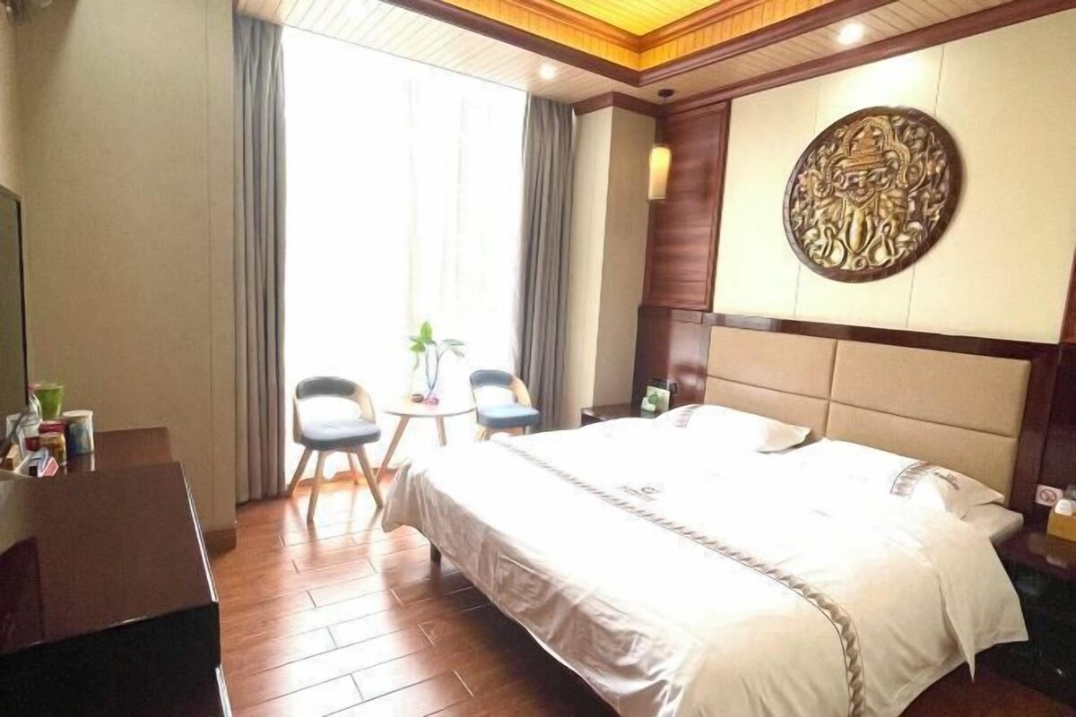 A hotel room with a large bed, a desk, two chairs, and a decorative wall piece.