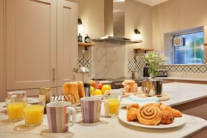 A breakfast setup with orange juice, croissants, and a fruit bowl on a marble countertop. - The Cottage at Tideswell (Tideswell)