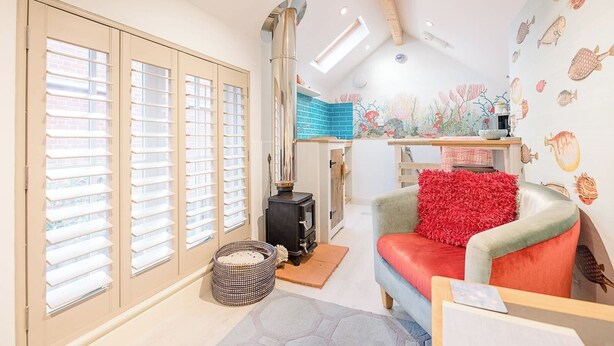 A cozy room with a fireplace, a sofa with a red cushion, and a wall decorated with fish illustrations. - The Fish Store, Aldeburgh (Aldeburgh)