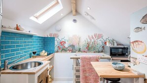 A kitchen with a blue tiled backsplash, wooden cabinets, a wooden dining table, and a mural of underwater scenery. - The Fish Store, Aldeburgh (Aldeburgh)