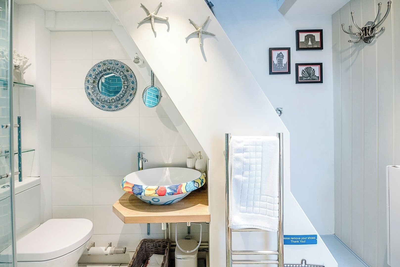 Une salle de bain avec un lavabo blanc, des toilettes et un espace douche. Les murs sont décorés d’étoiles de mer et on y trouve également des tableaux encadrés.