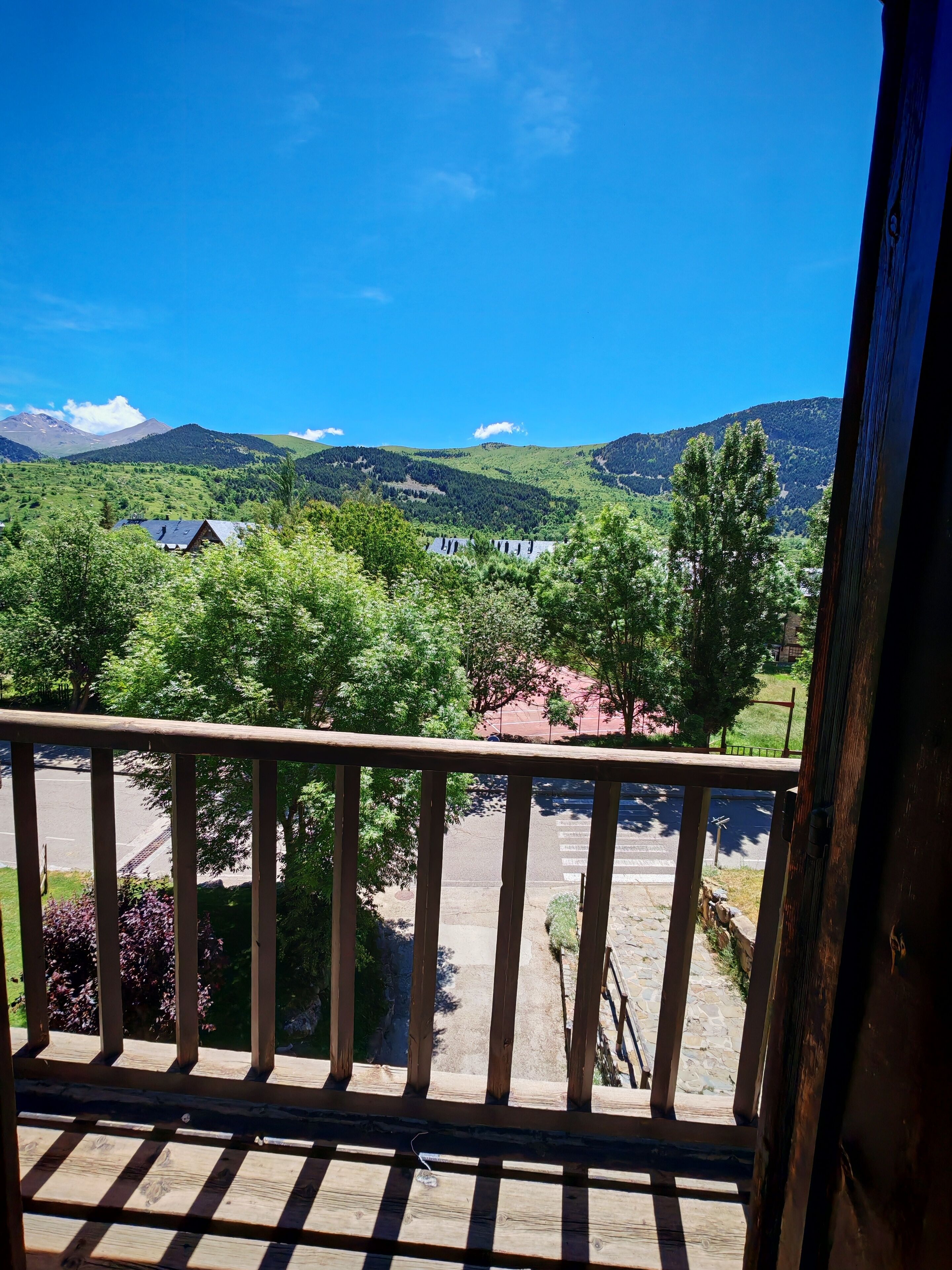 Ein Balkon mit Blick auf eine gebirgige Landschaft, eine gepflasterte Fläche mit einer Umzäunung und ein Gebäude in der Ferne.