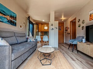 Un salon moderne avec un canapé gris, une table basse ronde et un téléviseur posé sur un meuble en bois.