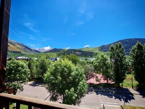 A view of a mountainous landscape with a clear sky, a road with a pedestrian crossing, and buildings in the foreground.