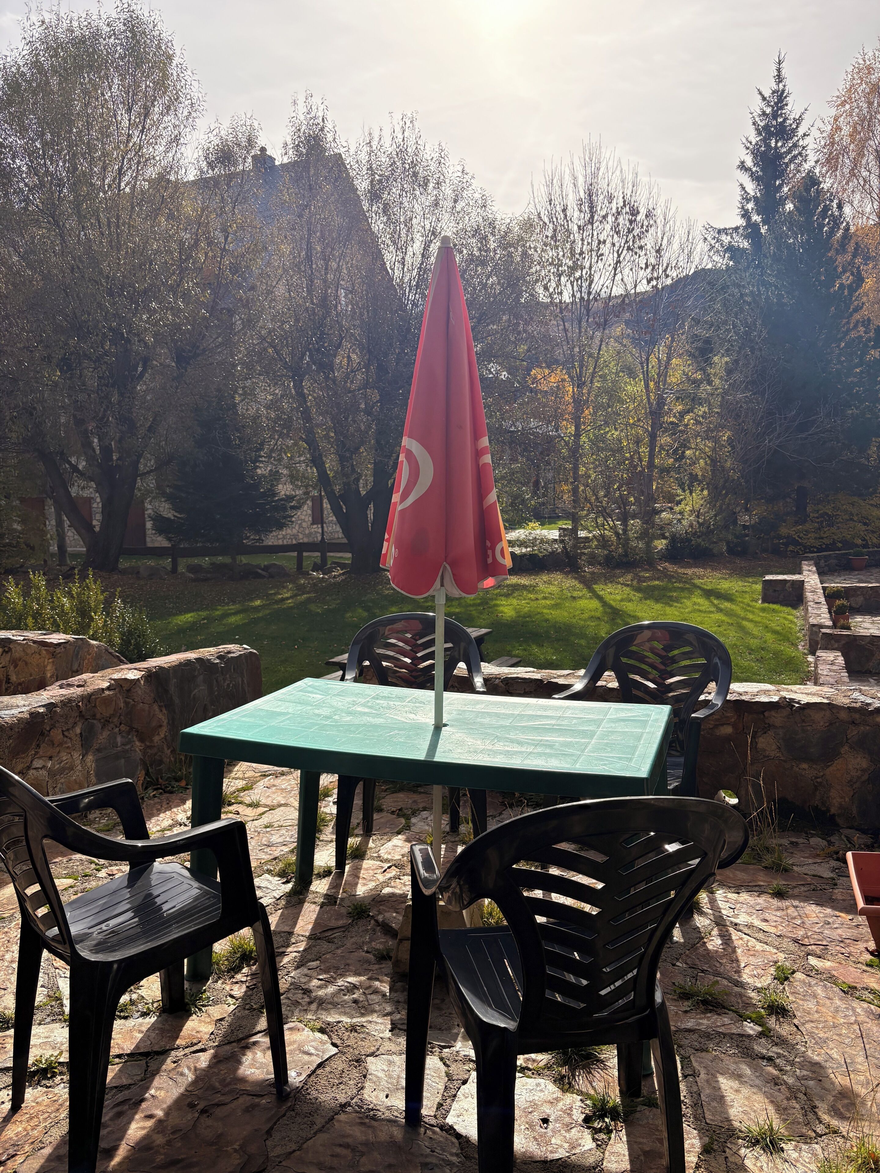 Eine Terrasse im Freien mit Tisch, Stühlen, einem roten Sonnenschirm und einer Steinmauer.