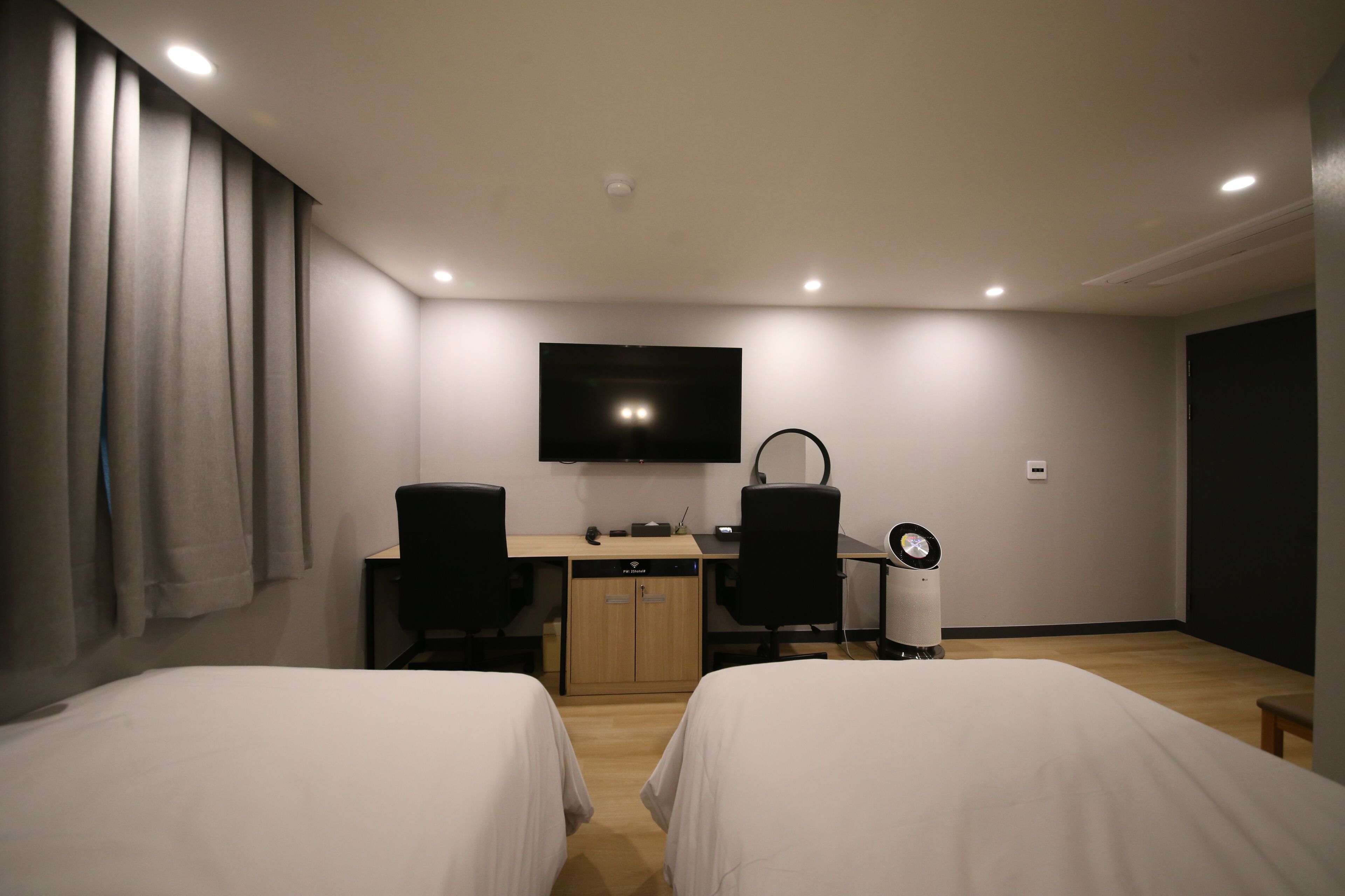 Une chambre d’hôtel avec deux lits, un bureau avec une chaise, une télévision et une petite table avec une horloge.