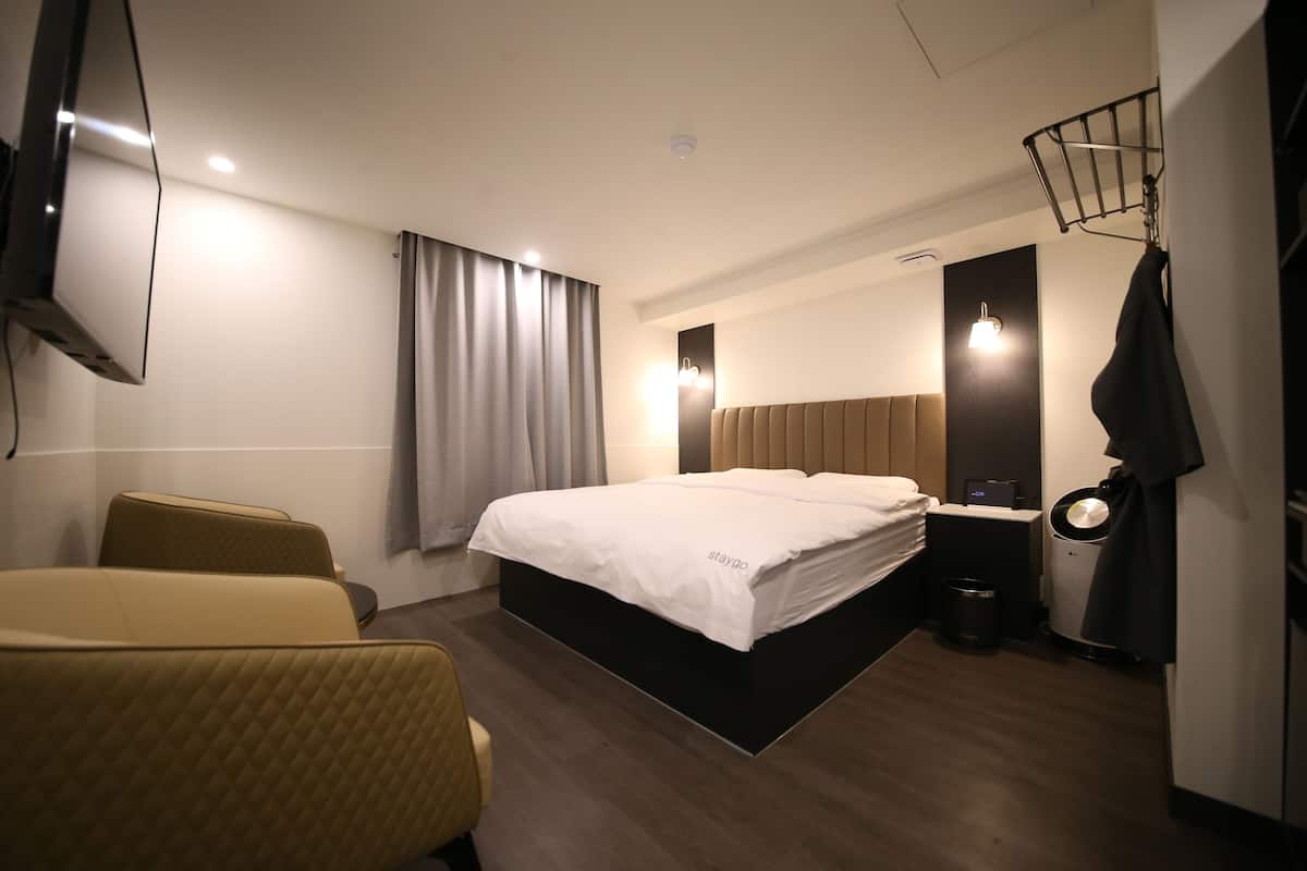 Una habitación de hotel con cama, televisor, escritorio y un cubo de basura.