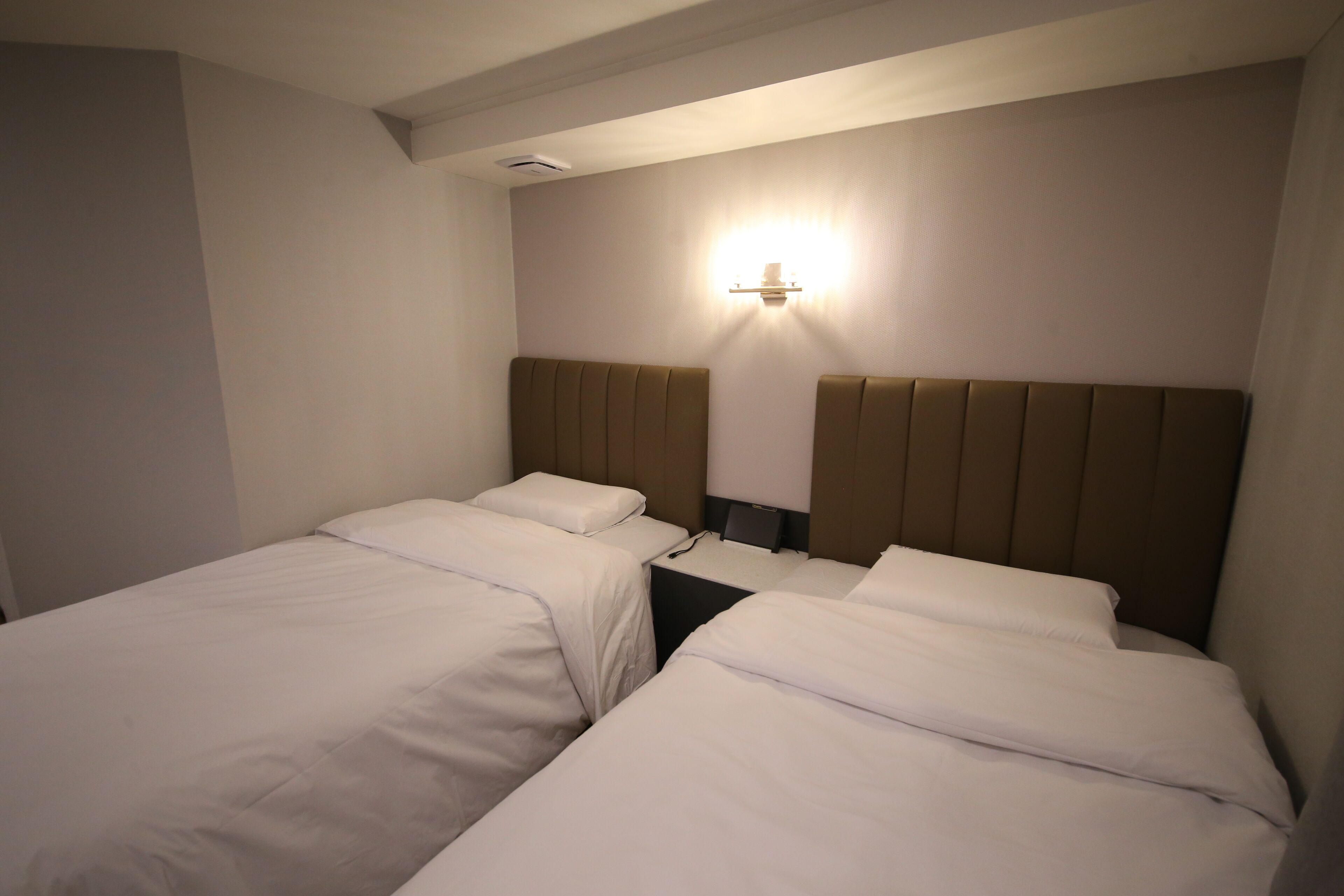 A hotel room with two single beds, a nightstand, and a wall-mounted light fixture.