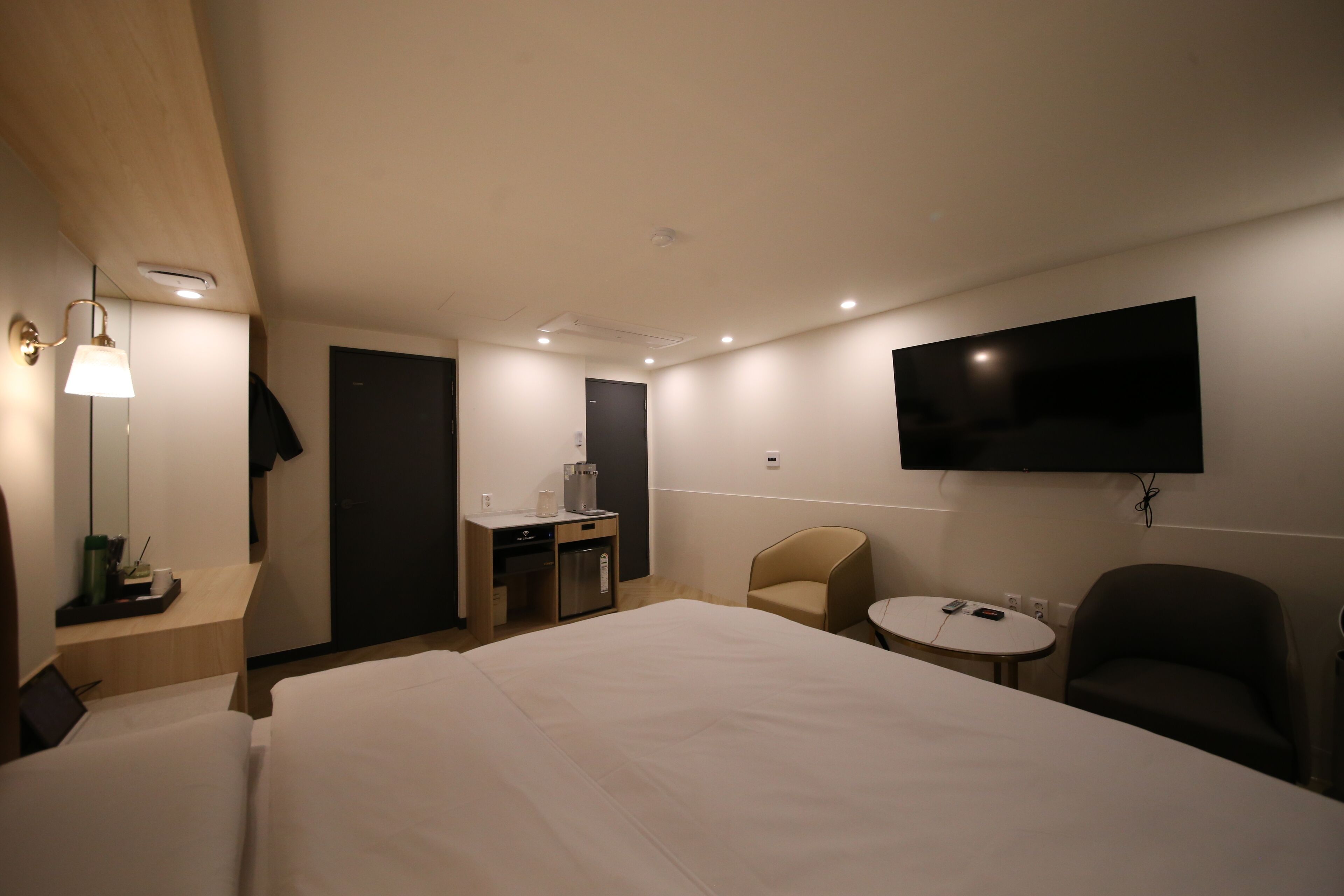 A hotel room with a large bed, a desk with a coffee machine, a TV mounted on the wall, and a small round table.