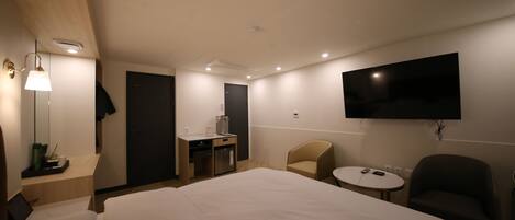 Une chambre d’hôtel avec un grand lit, un bureau avec une machine à café, un téléviseur fixé au mur et une petite table ronde.