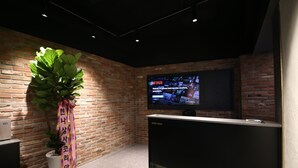 Un espace d’accueil avec un mur en briques, une plante en pot, un téléviseur diffusant Netflix et un comptoir de réception portant l’inscription « RÉCEPTION ».