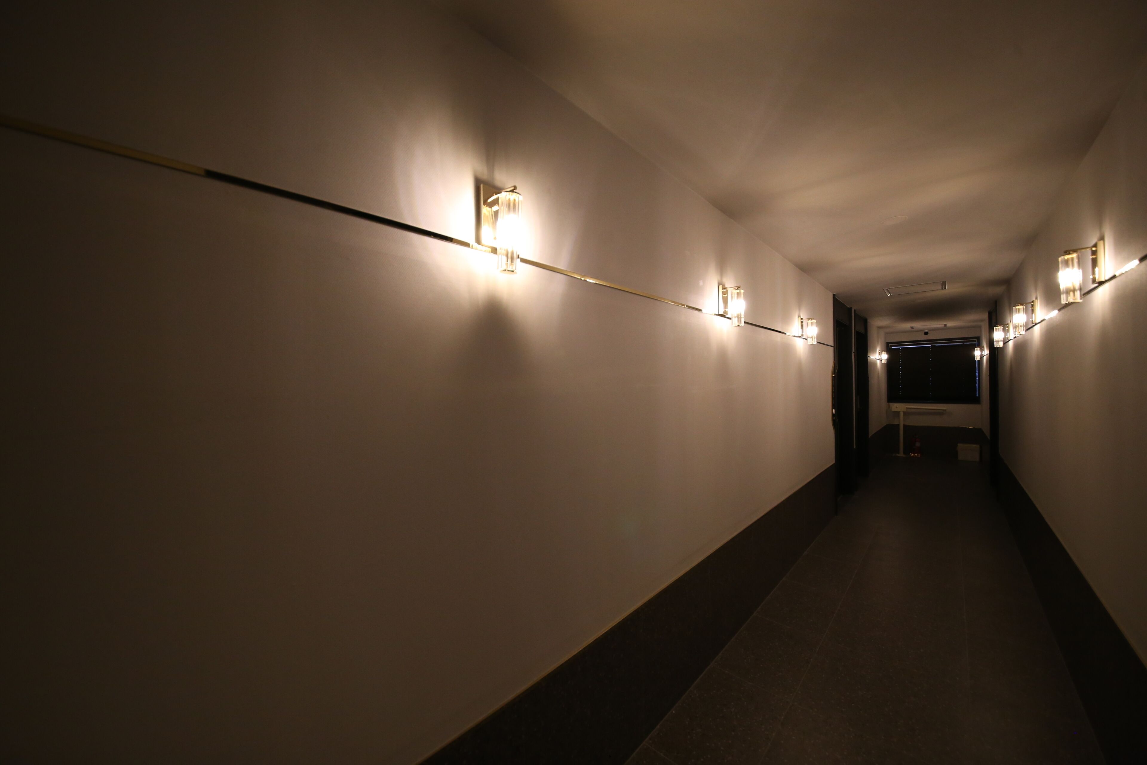 Un couloir avec des lampes fixées au mur et une porte au bout.