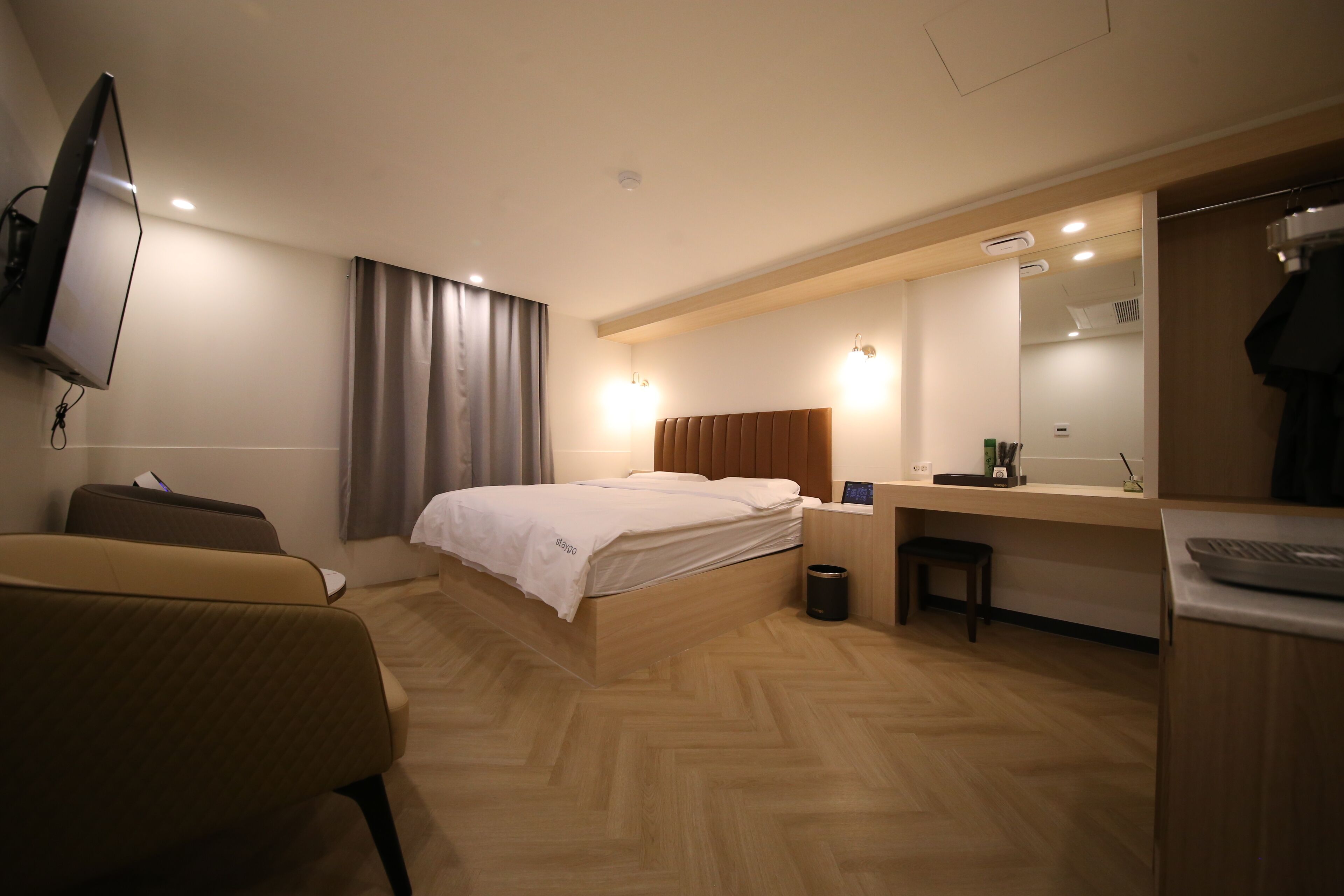 A hotel room with a bed, a desk, a chair, a TV, and a mirror.