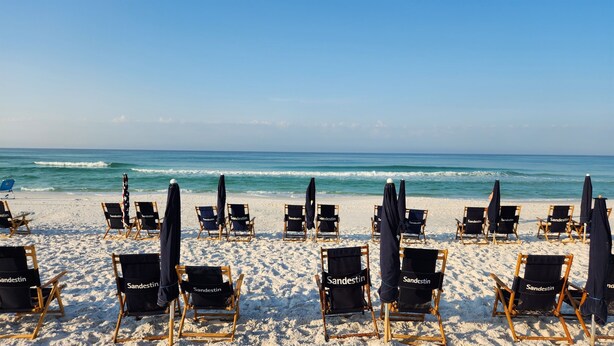 A beach with rows of black beach chairs and umbrellas labeled "Sandestin". - Luxury resort condo-10 th floor-Easy 4 min walk to beach, perfect time of year (Miramar Beach)