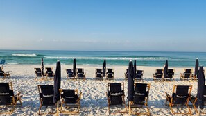 A beach with rows of black beach chairs and umbrellas labeled "Sandestin". - Luxury resort condo-10 th floor-Easy 4 min walk to beach, perfect time of year (Miramar Beach)