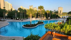 A swimming pool with lounge chairs and palm trees, surrounded by high-rise buildings. - Luxury resort condo-10 th floor-Easy 4 min walk to beach, perfect time of year (Miramar Beach)