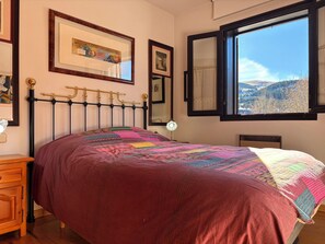Una cama con un edredón estampado, una mesita de noche, una lámpara y una ventana con vistas al paisaje.