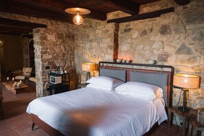 Un dormitorio con pared de piedra, estructura de cama de madera, dos lámparas de noche y una mesita con lámpara.