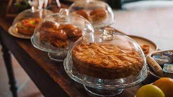 Una mesa de buffet con diversos alimentos cubiertos con campanas de cristal, incluyendo pasteles y pan.