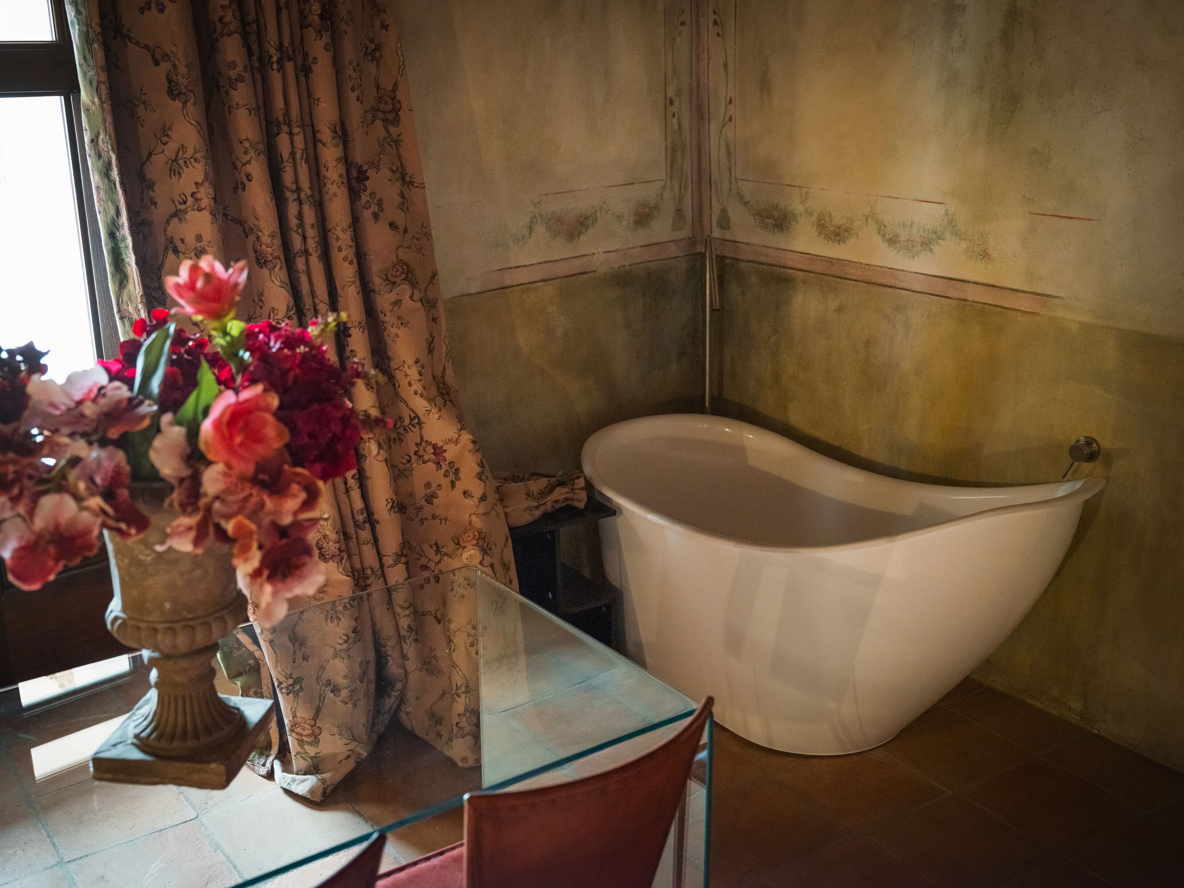 Un baño con una bañera, una mesa de vidrio y un florero con flores.