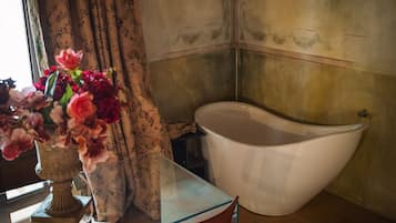 Un baño con una bañera, una mesa de vidrio y un florero con flores.
