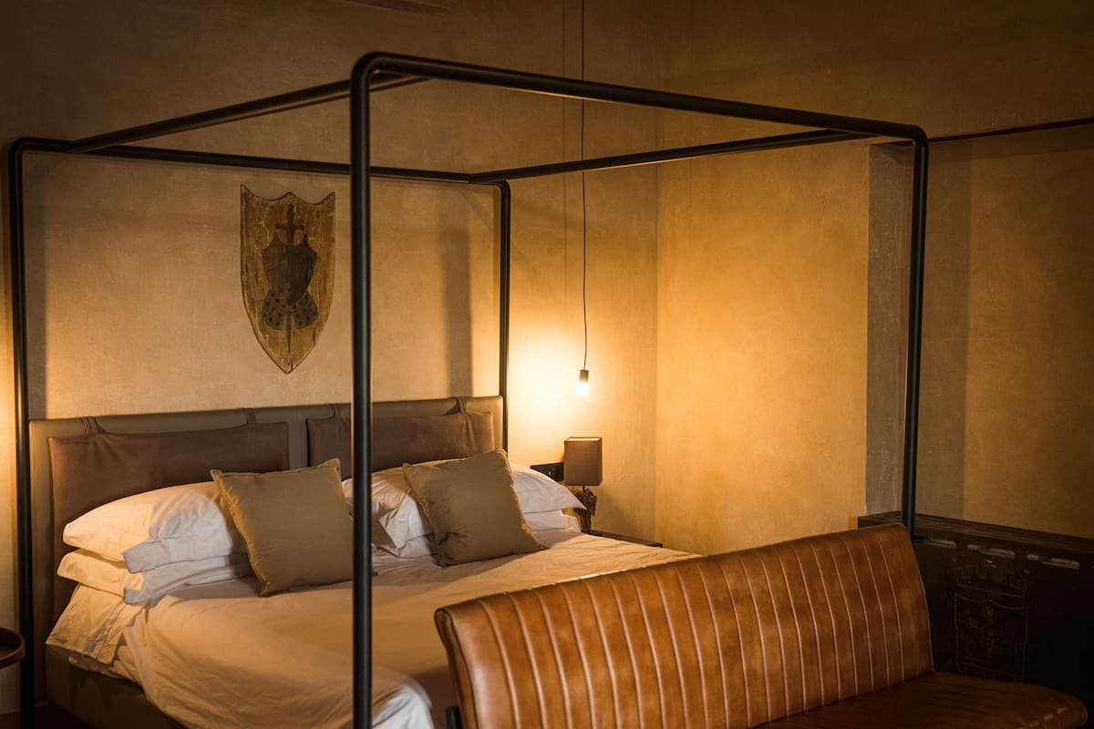 A four-poster canopy bed with a headboard, a bench, and a wall-mounted shield emblem.