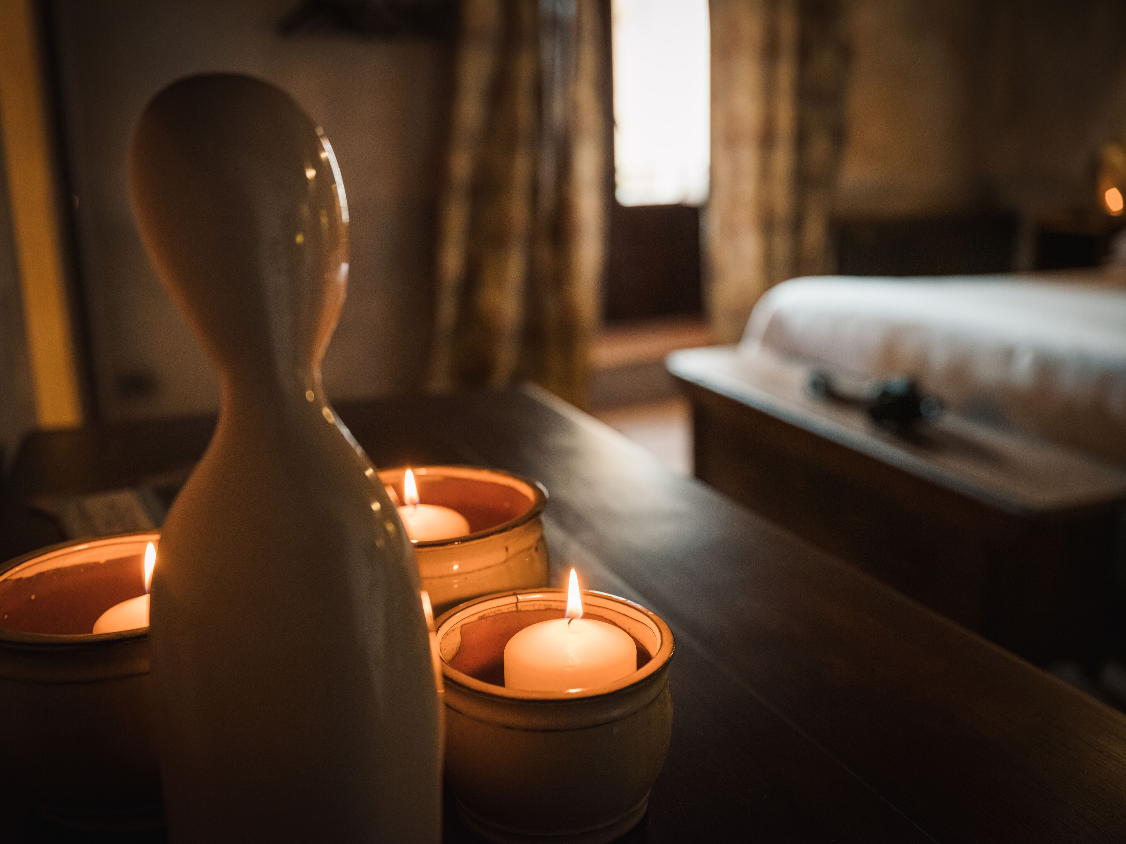 A room with a bed, a bedside table with candles, and a vase.