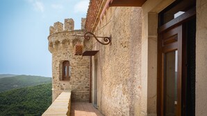 A stone building with a wooden door and window, a small balcony, and a view of a forested hill. - Castello di Rocca Cilento (Lustra)