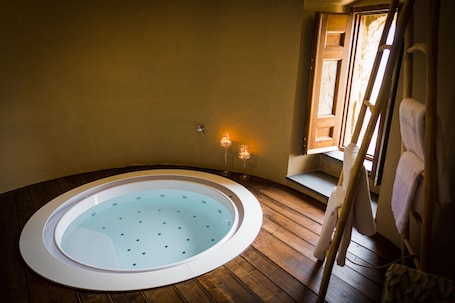 A hot tub in a wooden-floored room with a window and a towel rack.
